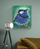 Canvas print of a blue bird painting on a wall with a lamp and sofa in the foreground.